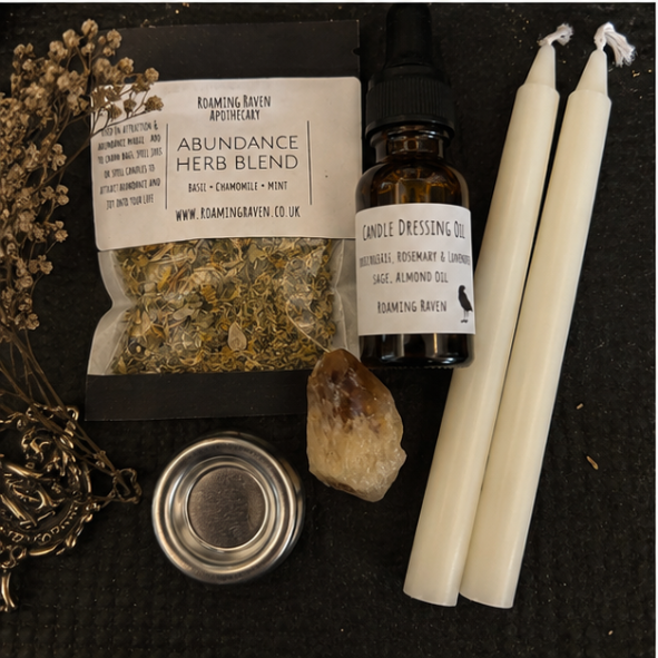 Close-up of abundance spell kit contents including abundance herb blend, white spell candles, herbal candle dressing oil, citrine crystal and metal candle holder.