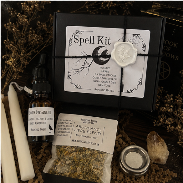 Close-up of abundance spell kit contents including abundance herb blend, white spell candles, herbal candle dressing oil, citrine crystal and metal candle holder.