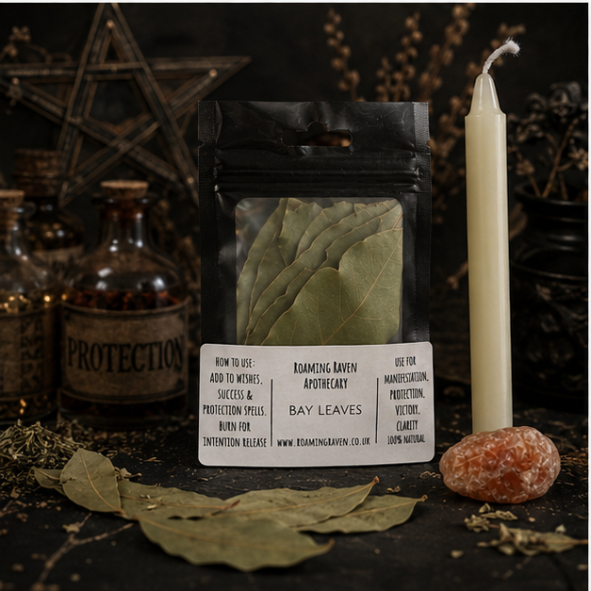 Close-up of dried bay leaves with ritual candle and red jade crystal surrounded by apothecary bottles and witchy décor on a dark altar.